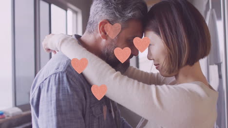 Animation-of-hearts-over-diverse-couple-embracing-and-smiling-at-home