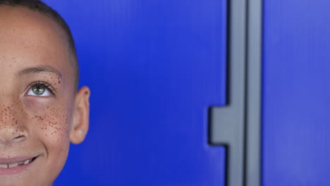 Biracial-boy-with-freckles-smiles-against-a-vibrant-blue-background-with-copy-space-in-school