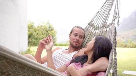 A-diverse-couple-relaxes-together-in-a-hammock-in-their-backyard-at-home