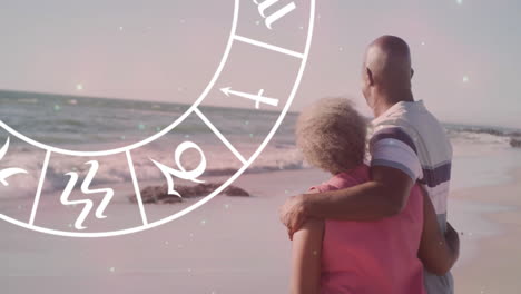 Animation-of-horoscope-moving-over-happy-senior-african-american-couple-embracing-at-beach