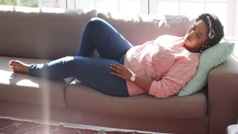 African-American-woman-rests-on-a-couch-at-home,-sunlight-streaming-in
