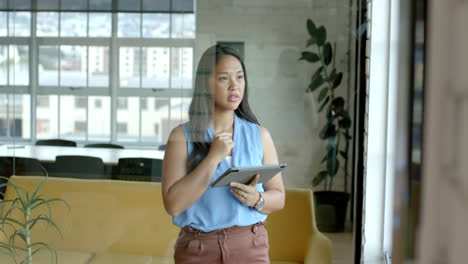 Middle-aged-Asian-businesswoman-holding-tablet,-looking-thoughtful