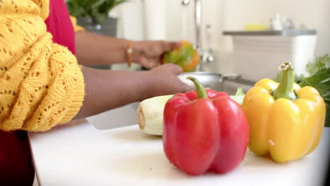 African-American-woman-prepares-food-at-home,-washing-a-bell-pepper-at-the-sink