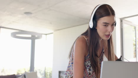 Teenage-Caucasian-girl-with-long-brown-hair-is-focused-on-her-laptop,-wearing-headphones