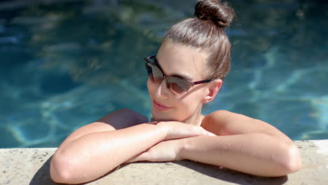 Una-Adolescente-Caucásica-Disfruta-De-La-Piscina,-Con-El-Pelo-Recogido-En-Un-Moño-Y-Gafas-De-Sol-Puestas.