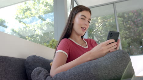 Teenage-Caucasian-girl-with-long-brown-hair,-wearing-a-red-and-white-shirt,-smiles-at-her-phone