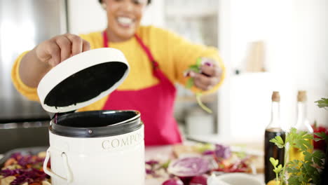 African-American-woman-adds-vegetable-scraps-to-a-compost-bin-in-a-bright-kitchen-at-home
