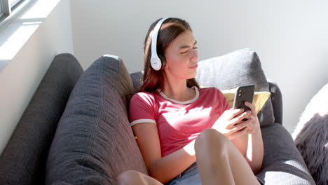 Teenage-Caucasian-girl-enjoys-music-on-her-headphones-while-using-a-smartphone-at-home