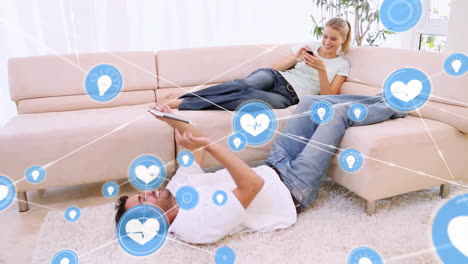 Animation-of-network-of-connections-with-icons-over-caucasian-couple-using-tablet-and-smartphone
