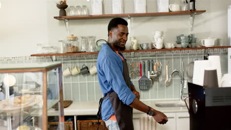 Young-African-American-male-barista-in-a-cafe,-tying-an-apron-around-his-waist