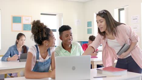 Diverse-teenagers-gather-around-laptop-in-a-bright-classroom