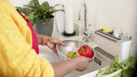 An-African-American-woman-rinses-vegetables-in-a-colander-at-a-kitchen-sink-at-home