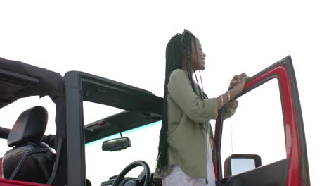 Young-African-American-woman-stands-by-a-red-convertible-on-a-road-trip,-enjoying-the-moment