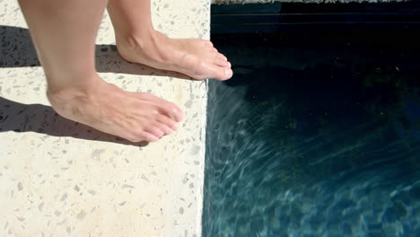 Bare-feet-are-poised-on-the-edge-of-a-swimming-pool,-ready-to-dip-into-the-water