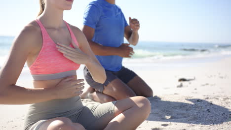 Young-Caucasian-woman-and-biracial-man-practice-yoga-on-a-sandy-beach