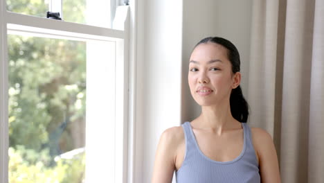 Young-biracial-woman-with-a-cheerful-smile-stands-by-a-window-with-copy-space