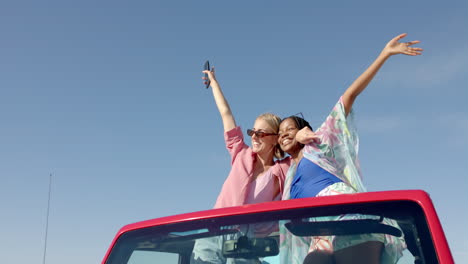 Young-African-American-woman-and-Caucasian-woman-celebrate-joyfully-in-a-red-car-on-a-road-trip