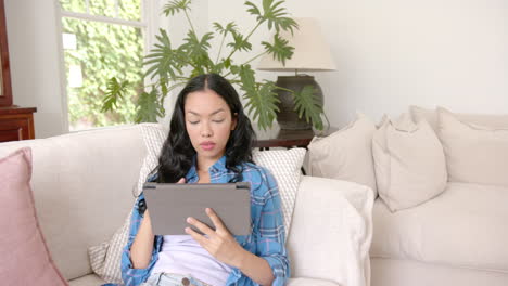 Young-biracial-woman-with-long-black-hair-holds-a-tablet,-smiling-at-camera