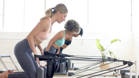 Dos-Mujeres-Practicando-En-Máquinas-Reformadoras-De-Pilates-En-Un-Estudio-Luminoso.