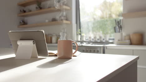 Steam-rising-from-hot-cup-on-kitchen-counter,-tablet-leaning-nearby