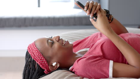 African-American-young-woman-lying-down,-holding-smartphone,-laughing
