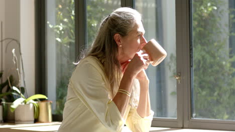 Caucasian-mature-woman-drinking-coffee-by-window