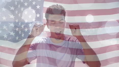 Animation-of-light-spots-and-american-flag-over-happy-biracial-man-dancing-on-sunny-beach