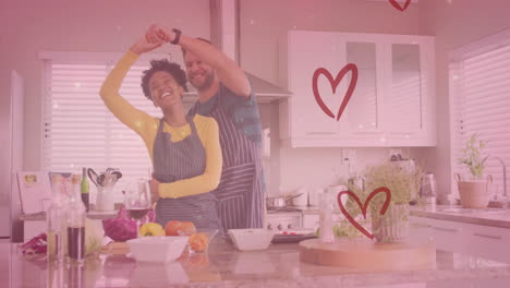 Animation-of-hearts-over-diverse-couple-dancing-in-kitchen-at-home
