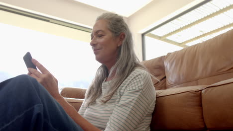 Caucasian-mature-woman-sitting-on-sofa,-looking-at-smartphone