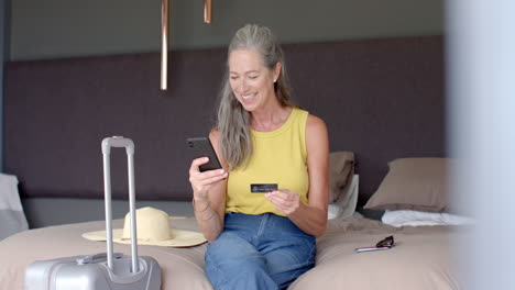 Mujer-Caucásica-Con-Pelo-Gris,-Sentada,-Sosteniendo-Una-Tarjeta-De-Crédito-Y-Un-Teléfono-Inteligente