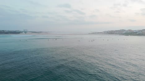 Toma-De-Seguimiento-Aéreo-Mostrando-A-Un-Grupo-De-Surfistas-En-El-Océano-Atlántico-Al-Atardecer.