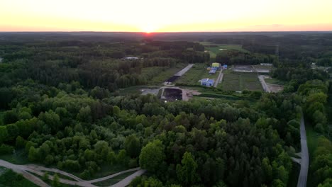 Panorama-Del-Atardecer,-Vista-Del-Paisaje-Con-Un-Bosque,-Edificios-Rurales-Y-La-Puesta-De-Sol