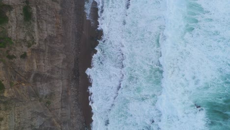 Océano-Enormes-Olas-Turquesas-Rompiendo-Al-Atardecer-En-Una-Playa-De-Arena-Rodeada-De-Acantilados