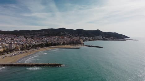 Costa-De-Sitges-Y-Paisaje-Urbano-Con-Montañas-Al-Fondo,-Vista-Aérea