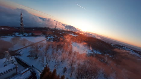 FPV-drone-flies-over-snowy-landscape-with-communication-towers-at-sunset
