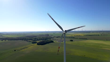 View-of-spinning-wind-turbine-blades-against-the-backdrop-of-a-rapeseed-field,-renewable-energy-source