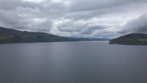 Aerial-circling-small-boat-sailing-on-Loch-Ness-on-cloudy-day,-Scotland