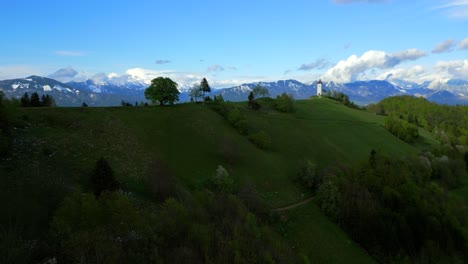 Picturesque-scene-of-the-iconic-Jamnik-church,-poised-amidst-the-verdant-Slovenian-hills,-under-embrace-of-a-partly-cloudy-sky