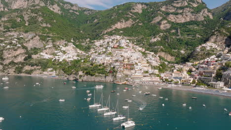 Aérea:-Vista-Panorámica-De-Positano-En-La-Costa-De-Amalfi,-Italia-Con-Yates-Junto-A-La-Costa-Durante-Un-Día-Soleado