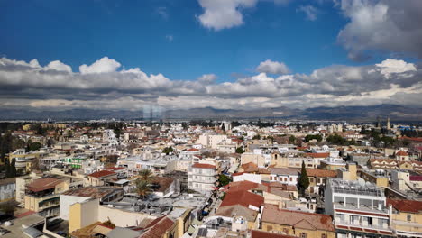 N-Vista-Elevada-De-Nicosia,-Chipre,-Destacando-La-Combinación-De-Edificios-Residenciales-Y-Comerciales-Con-Un-Telón-De-Fondo-De-Montañas-Y-Nubes