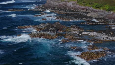 Aerial-tracking-pan-follows-strong-crashing-waves-spread-whitewash-over-rocky-coastal-shores-of-Hookipa-Maui