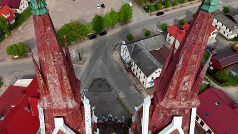 Red-roofed-church-towers-in-a-lithuanian-village,-surrounded-by-buildings-and-streets,-aerial-view