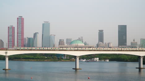 Train-Travels-on-Dangsan-Railway-Bridge-Crossing-Han-River-in-Seoul-with-National-Assembly-of-the-Republic-of-Korea-and-Downtown-of-Yeouido-Financial-District-in-Backdrop,-Yeongdeungpo-gu---zoom-out