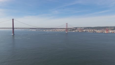 Aerial-tilt-up-shot-on-ponte-25-de-Abril-with-a-plane-passing-by-during-sunny-day