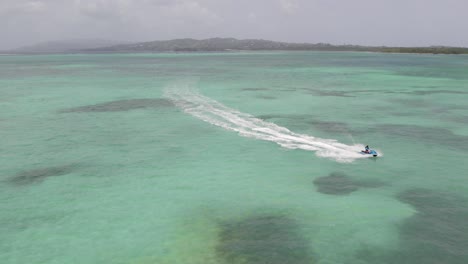 A-girl-on-a-jetski-in-nylon-pool,-Tobago-aerial-drone-view