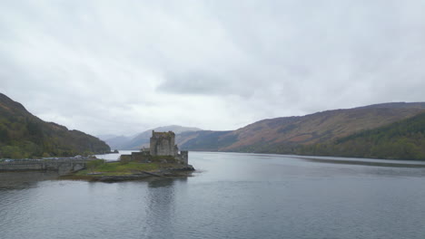 Aerial-flying-backwards-from-Eilean-Donan-Castle-on-cloudy-day,-Scotland