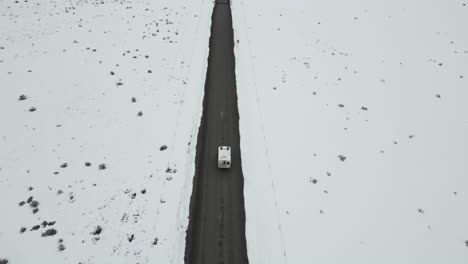 Aerial-of-a-white-camper-van-navigating-through-the-wintry,-desolate-landscape-of-Idaho,-USA