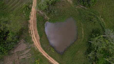-Drone-flying-over-water-pond-and-dirt-road