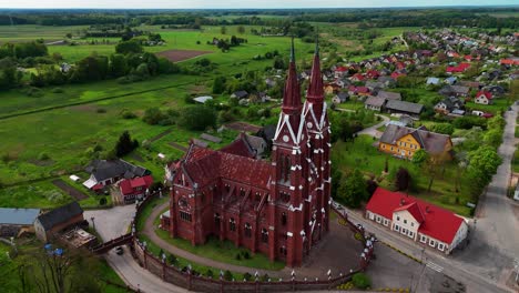 Sveksna-church-in-lithuania-with-surrounding-countryside-and-colorful-buildings,-aerial-view