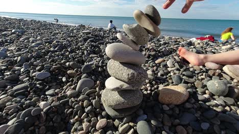 La-Torre-Se-Construyó-Equilibrando-Piedras-De-Guijarros-Una-Encima-De-Otra-Hasta-Que-Colapsan-En-El-Fondo,-Podemos-Ver-Los-Pies-De-Varias-Personas-Y-Niños.